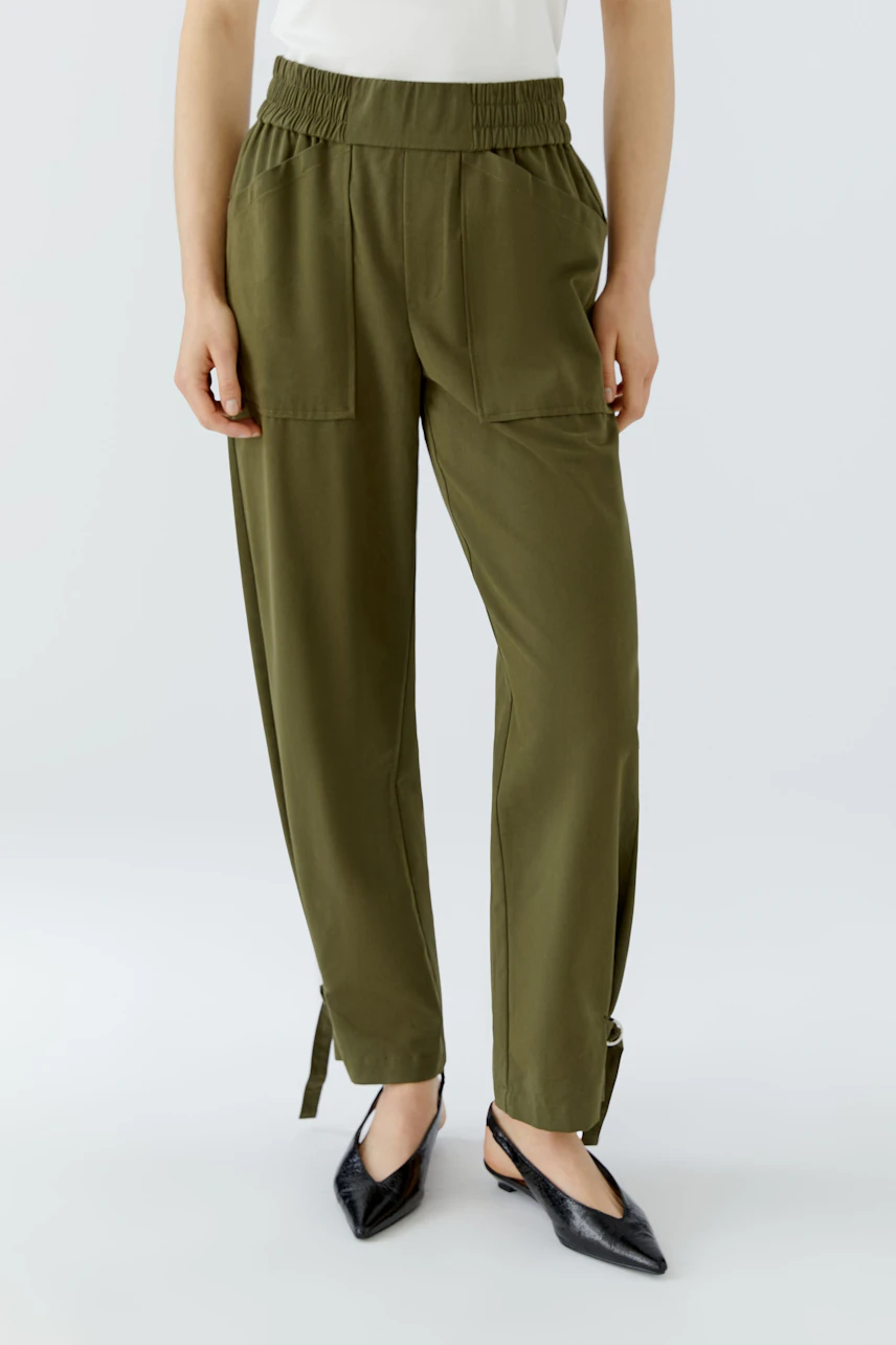 Casual women's pants: Woman in olive green pants with elastic waistband and side pockets, wearing black shoes.