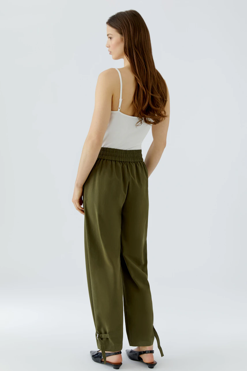Casual women's pants: Woman in olive green pants with a white top, viewed from the back.