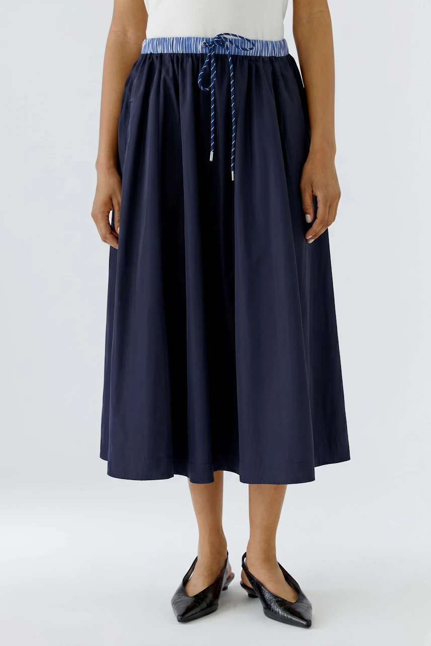 Woman in a navy midiskirt with a drawstring waist, paired with black shoes, standing confidently.