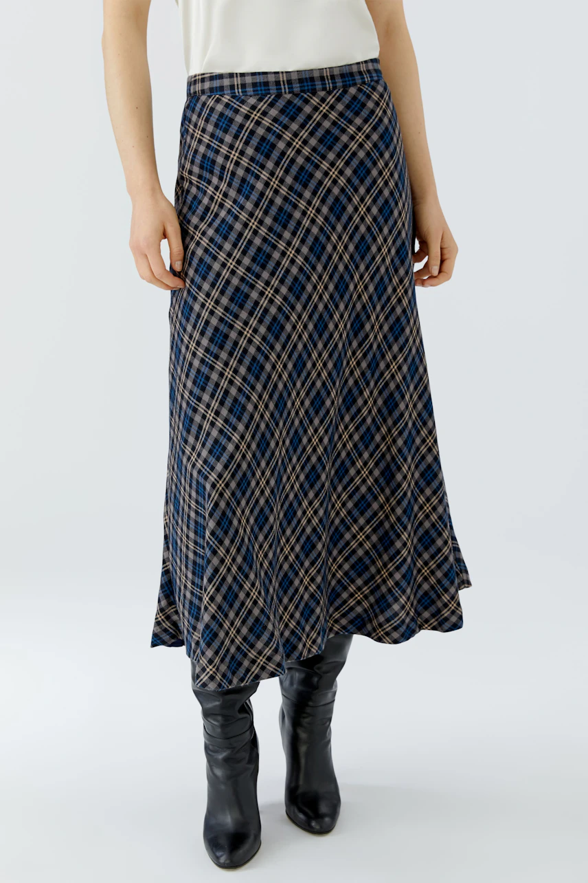 A-line skirt: Woman in a plaid A-line skirt with a white top and black boots.