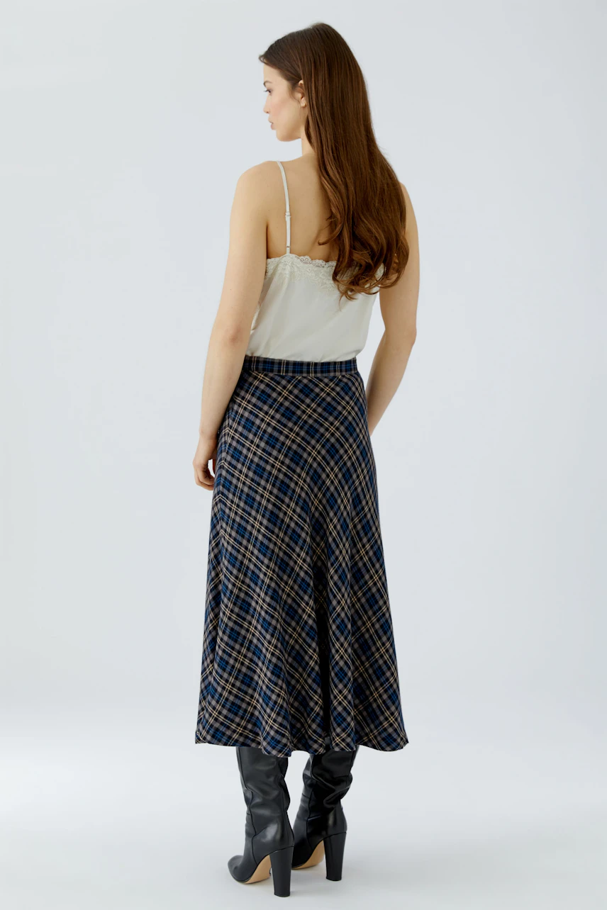 A-line skirt: Woman in a plaid A-line skirt, white top, and black boots, viewed from the back.