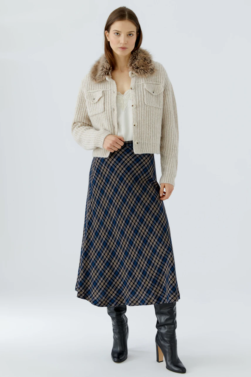 A-line skirt: Woman in a plaid A-line skirt, cream cardigan with fur collar, and black boots.