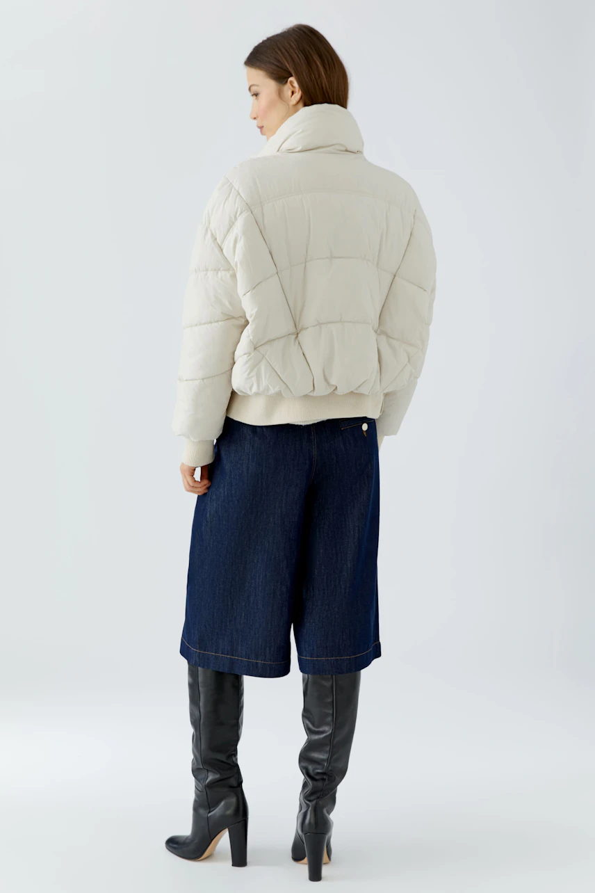 Outdoorjacke: Frau in cremefarbener Jacke, kombiniert mit blauen Culottes und schwarzen Stiefeln.
