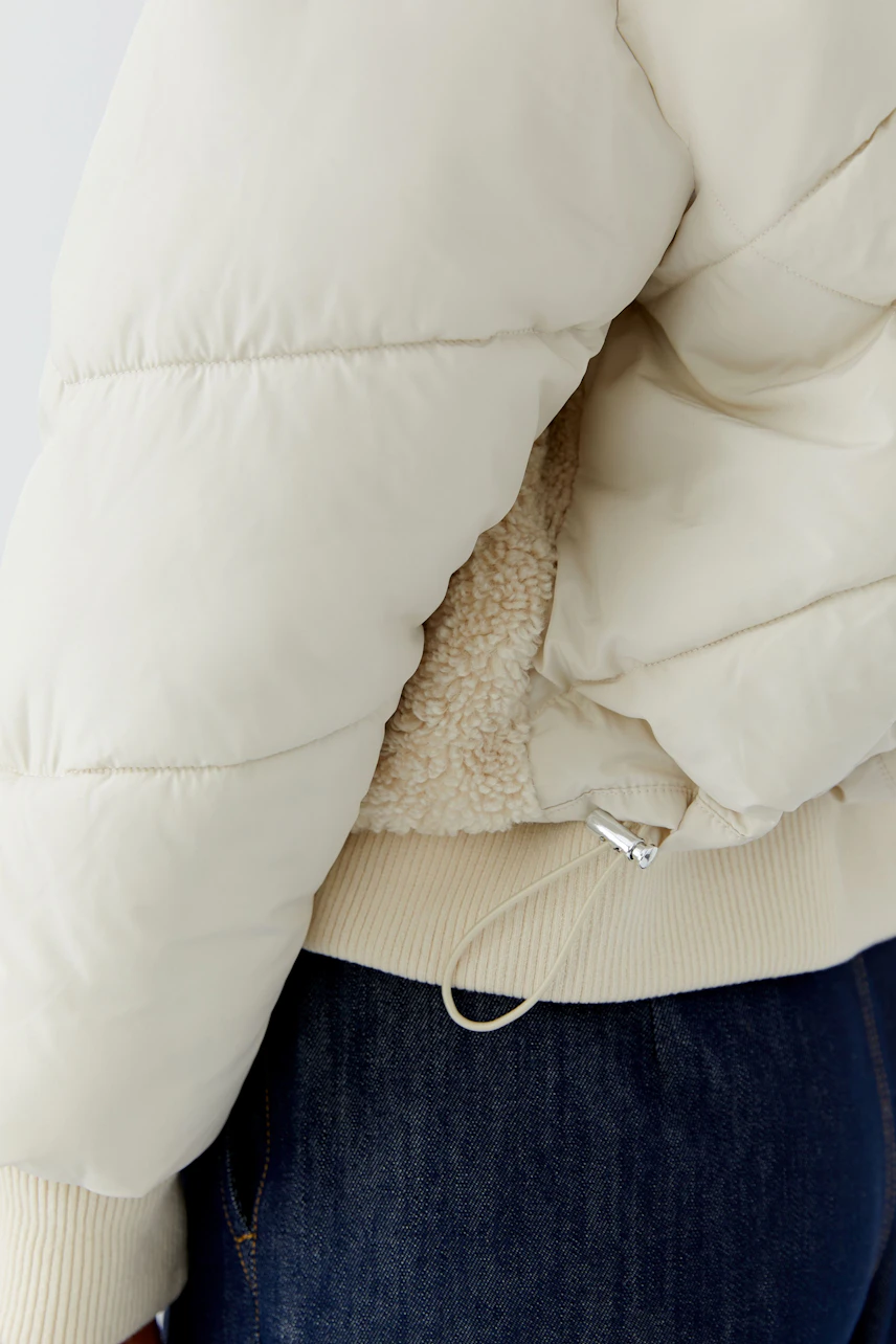Outdoorjacke: Cremefarbene Jacke mit Teddyfutter und Kordelzug, kombiniert mit dunkler Jeans.