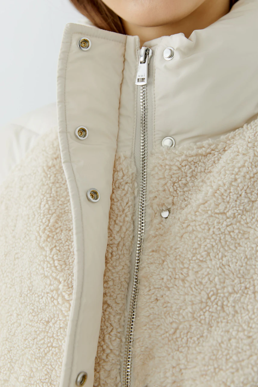 Outdoorjacke: Frau in cremefarbener Jacke mit weichem Fleece und Reißverschluss.