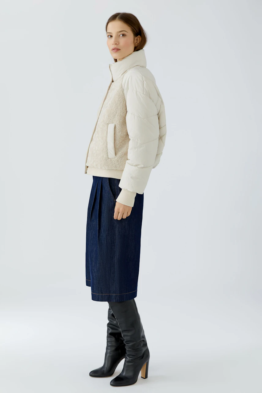 Outdoorjacke: Frau in beiger Jacke mit Stehkragen, kombiniert mit dunklem Rock und schwarzen Stiefeln.