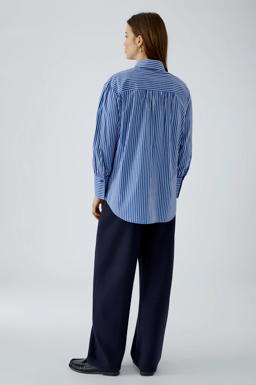 Striped shirt blouse: Woman in blue and white striped blouse with loose navy trousers, looking away.