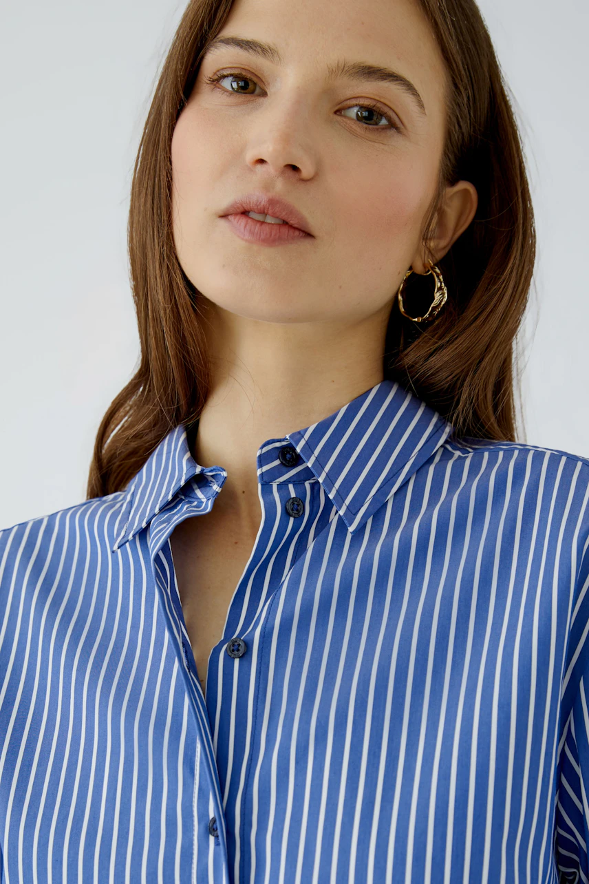 Striped shirt blouse: Woman in blue and white striped blouse with open collar, looking confidently.