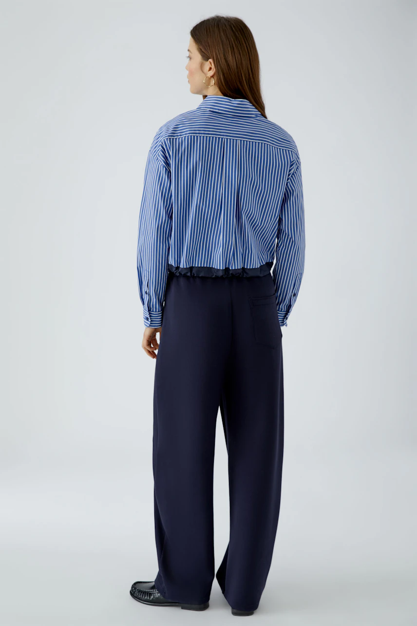 Striped shirt blouse: Woman in blue and white striped blouse with loose navy pants, viewed from the back.