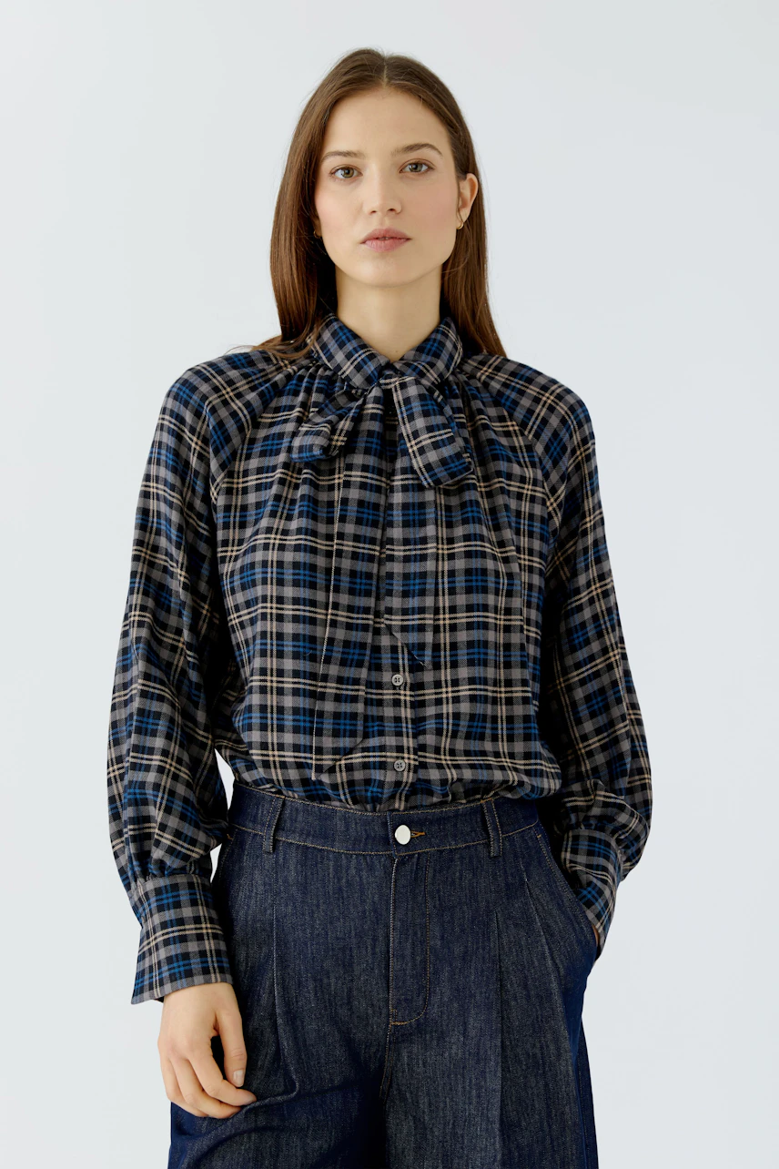 Casual women's blouse: Woman in a plaid blouse with a bow tie detail, paired with dark denim jeans.