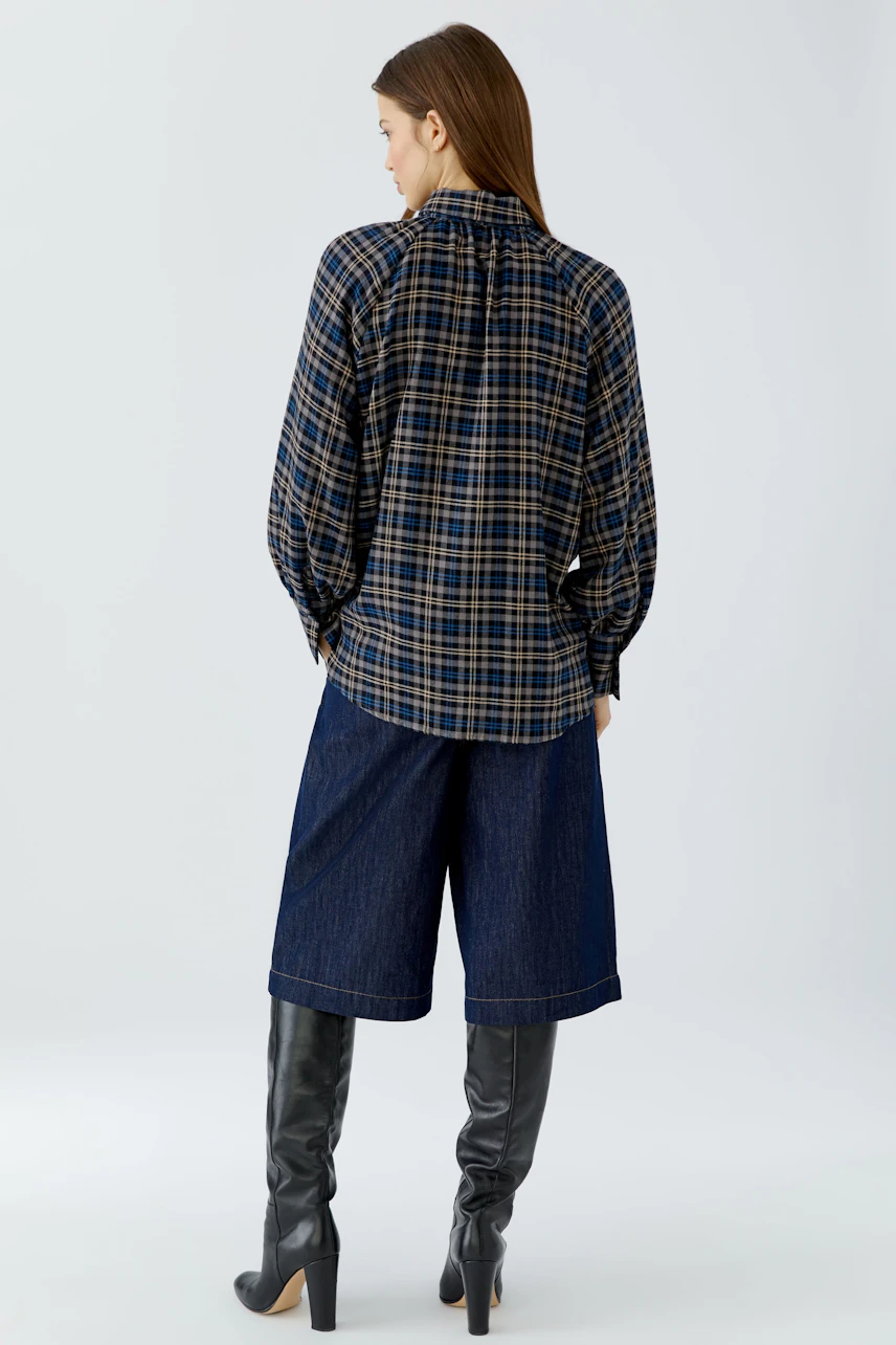 Casual women's blouse: Woman in a plaid blouse with wide denim culottes and knee-high boots, facing away.