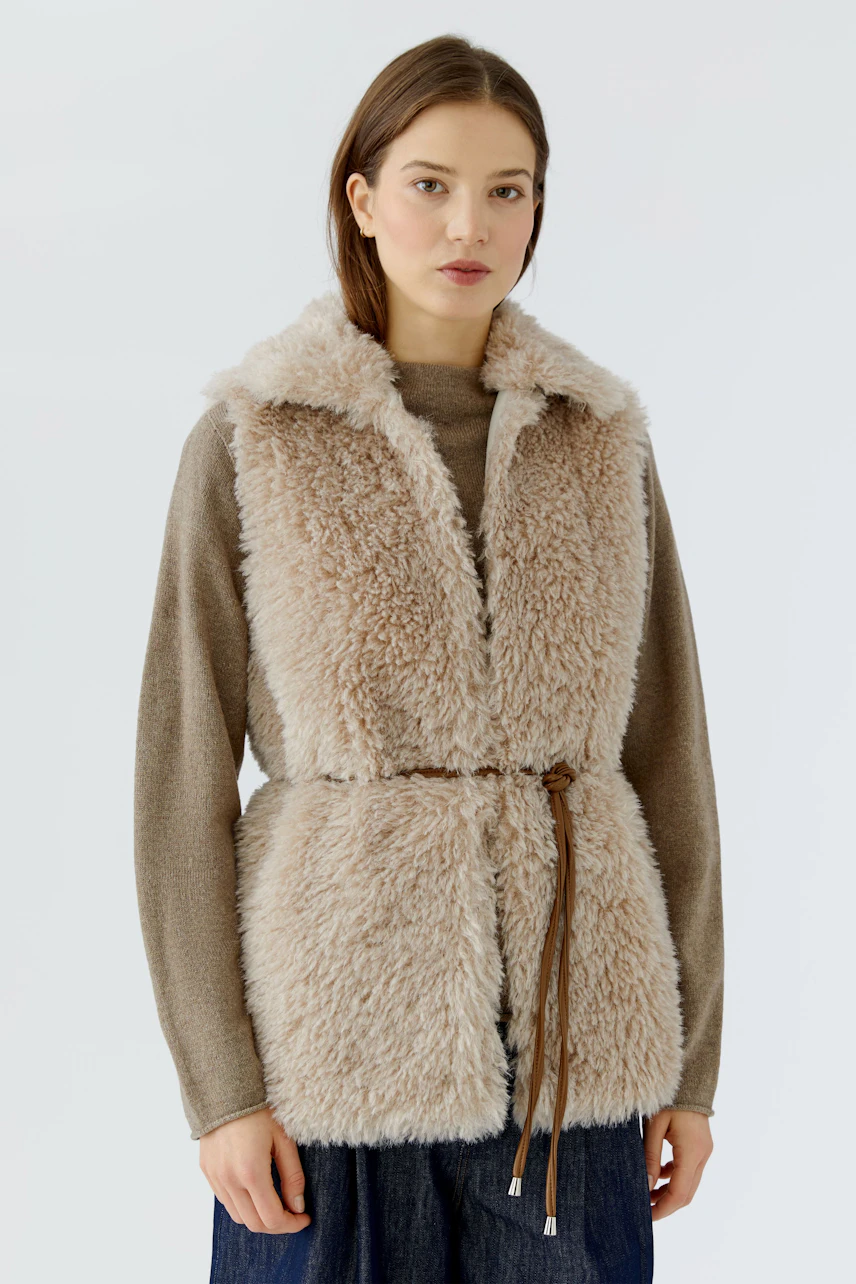 Woman in cozy beige vest over brown pullover, paired with jeans. Casual and warm look.