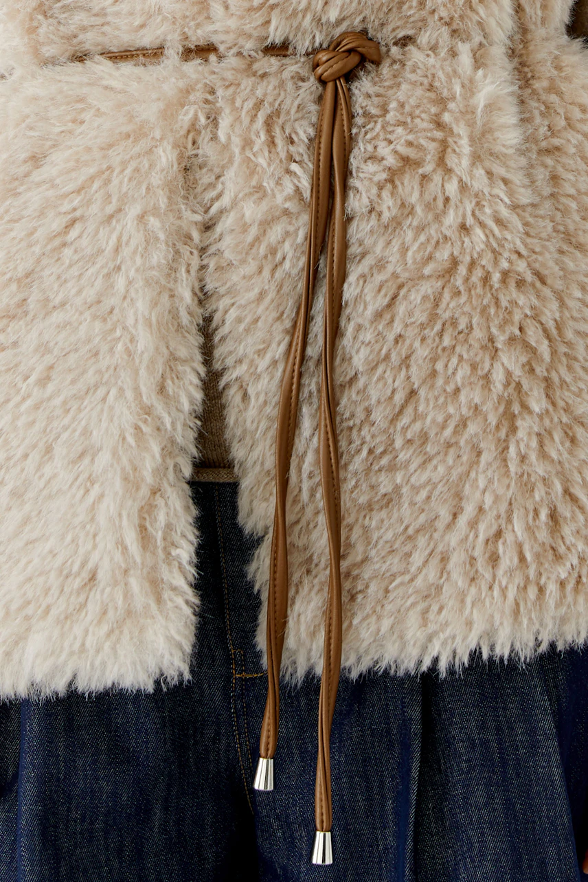 Cozy faux fur vest with brown tie detail over denim. Perfect for layering and adding texture to any outfit.