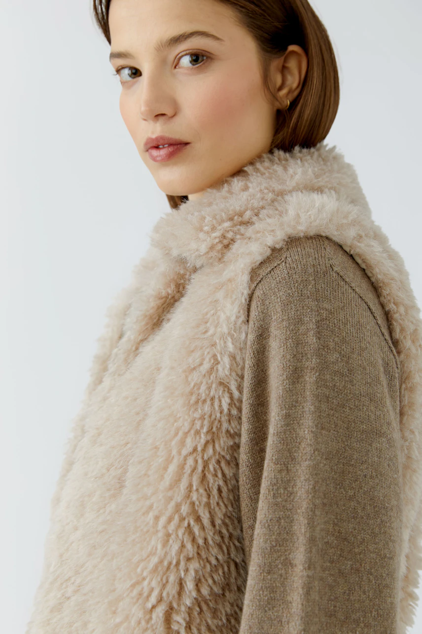 Woman in cozy beige vest over a brown sweater, looking confidently to the side.