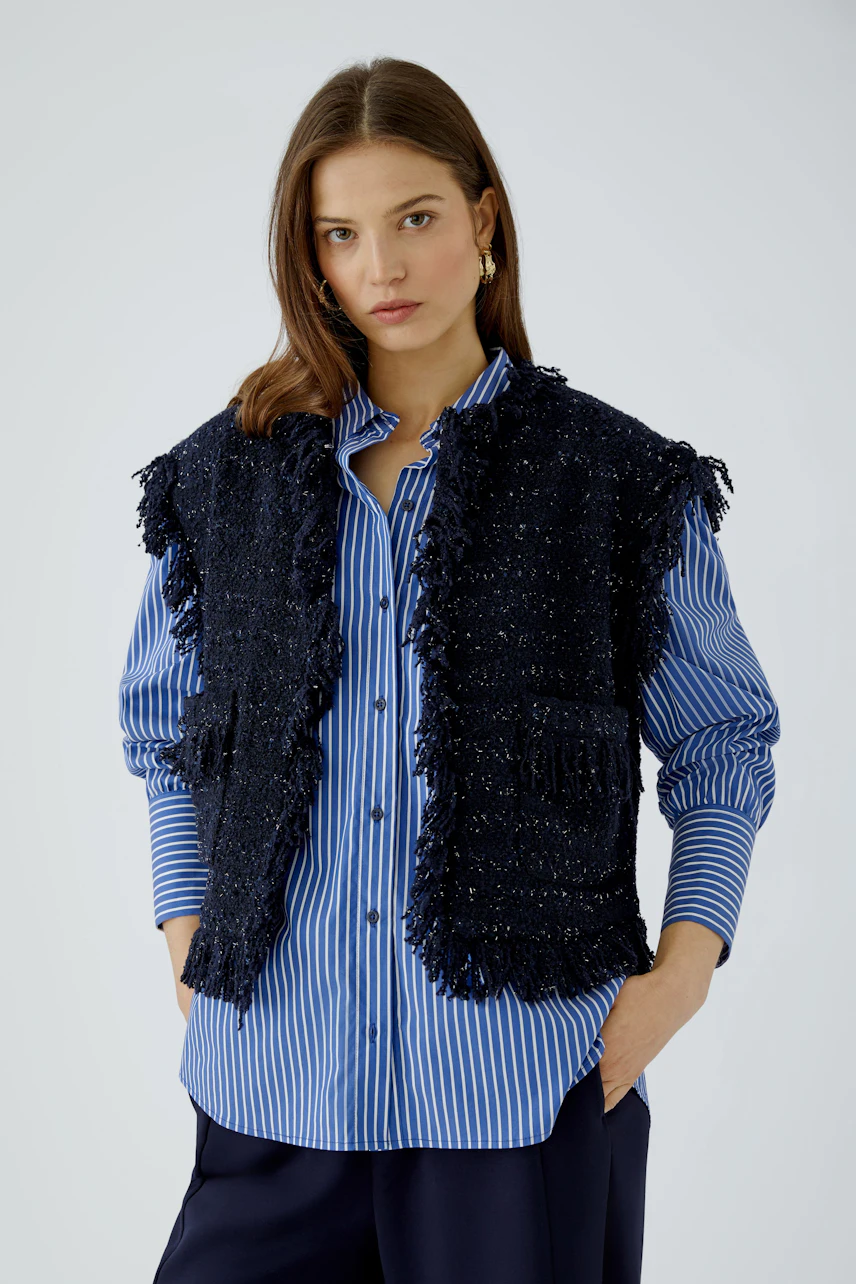 Casual women's vest: Woman in a textured black vest over a blue striped shirt, looking confidently.