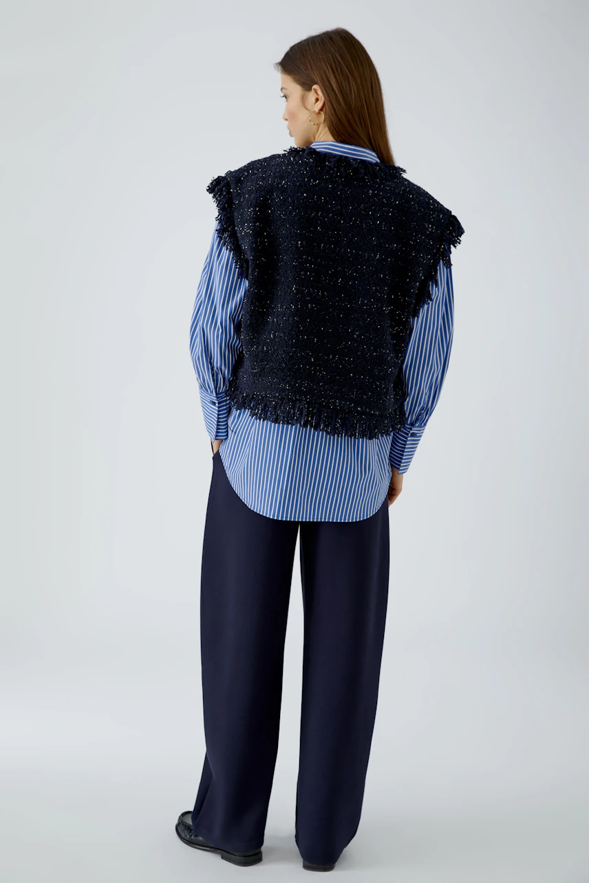 Casual women's vest: Woman in a textured black vest over a blue striped shirt, paired with navy trousers.