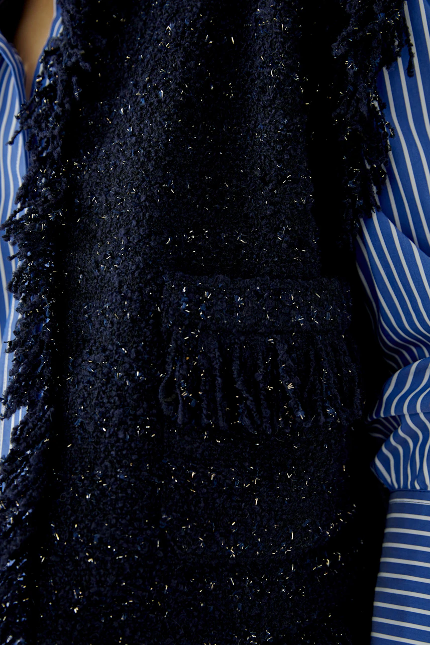 Textured women's vest: Close-up of a dark, fringed vest over a blue striped shirt.
