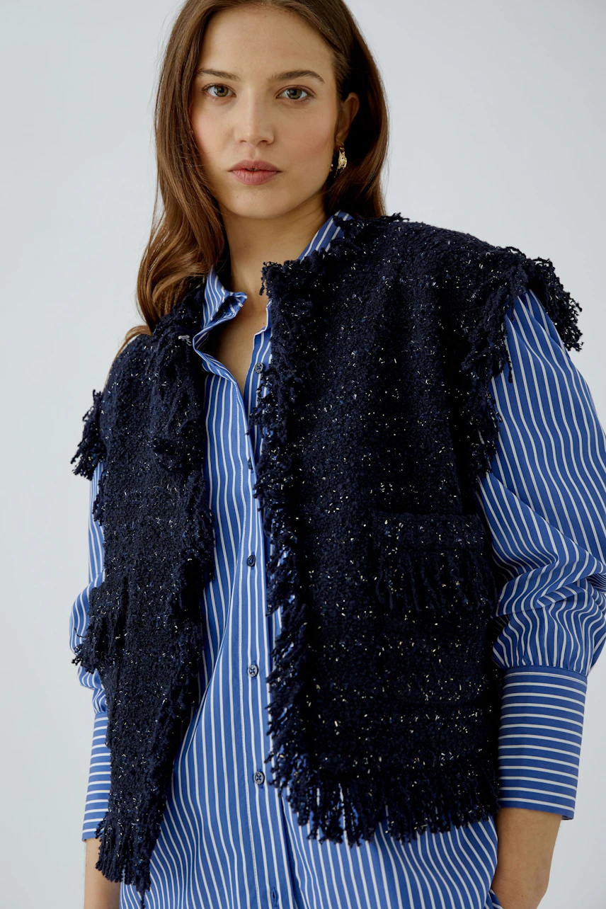Casual women's vest: Woman in a textured black vest over a blue striped shirt, looking confidently.