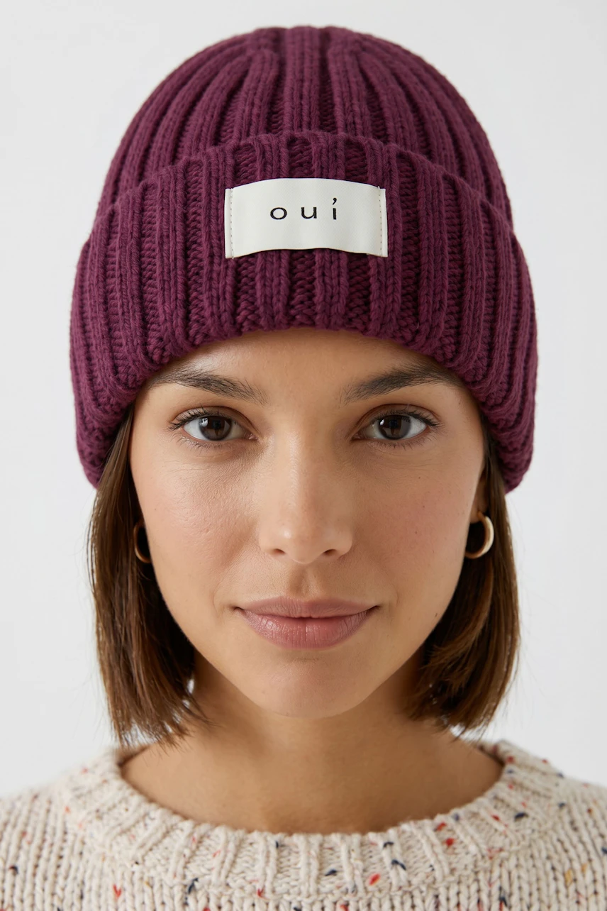 Frau mit lila Mütze von Oui, lächelt dezent. Strickdesign mit Logo-Patch, ideal für kalte Tage.