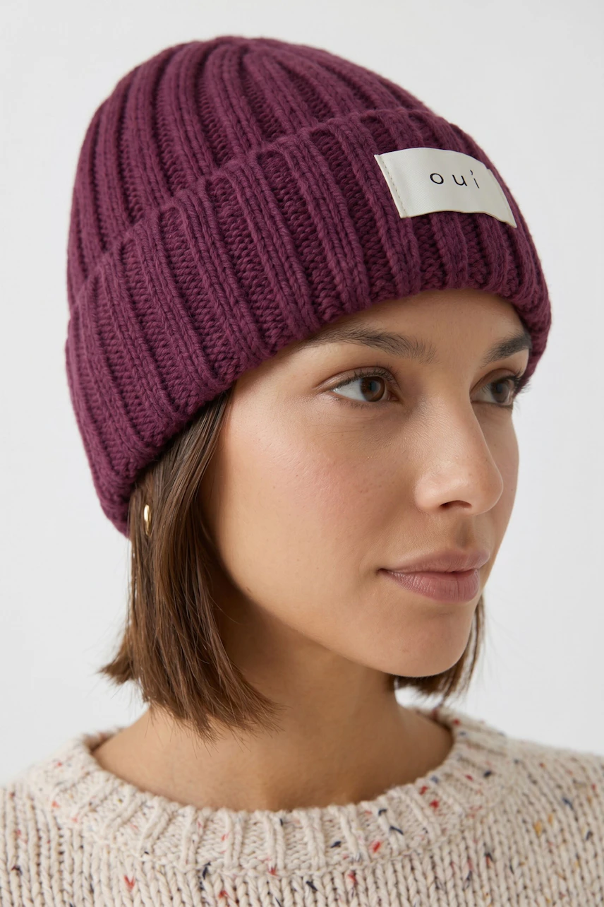 Frau mit lila Mütze von Oui, trägt einen cremefarbenen Pullover. Schlichtes, modernes Design.