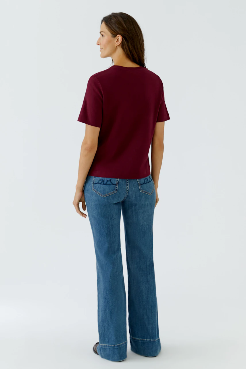 Frau im weinroten T-Shirt und blauen Jeans, Rückansicht. Schlichtes Design für lässigen Alltagslook.