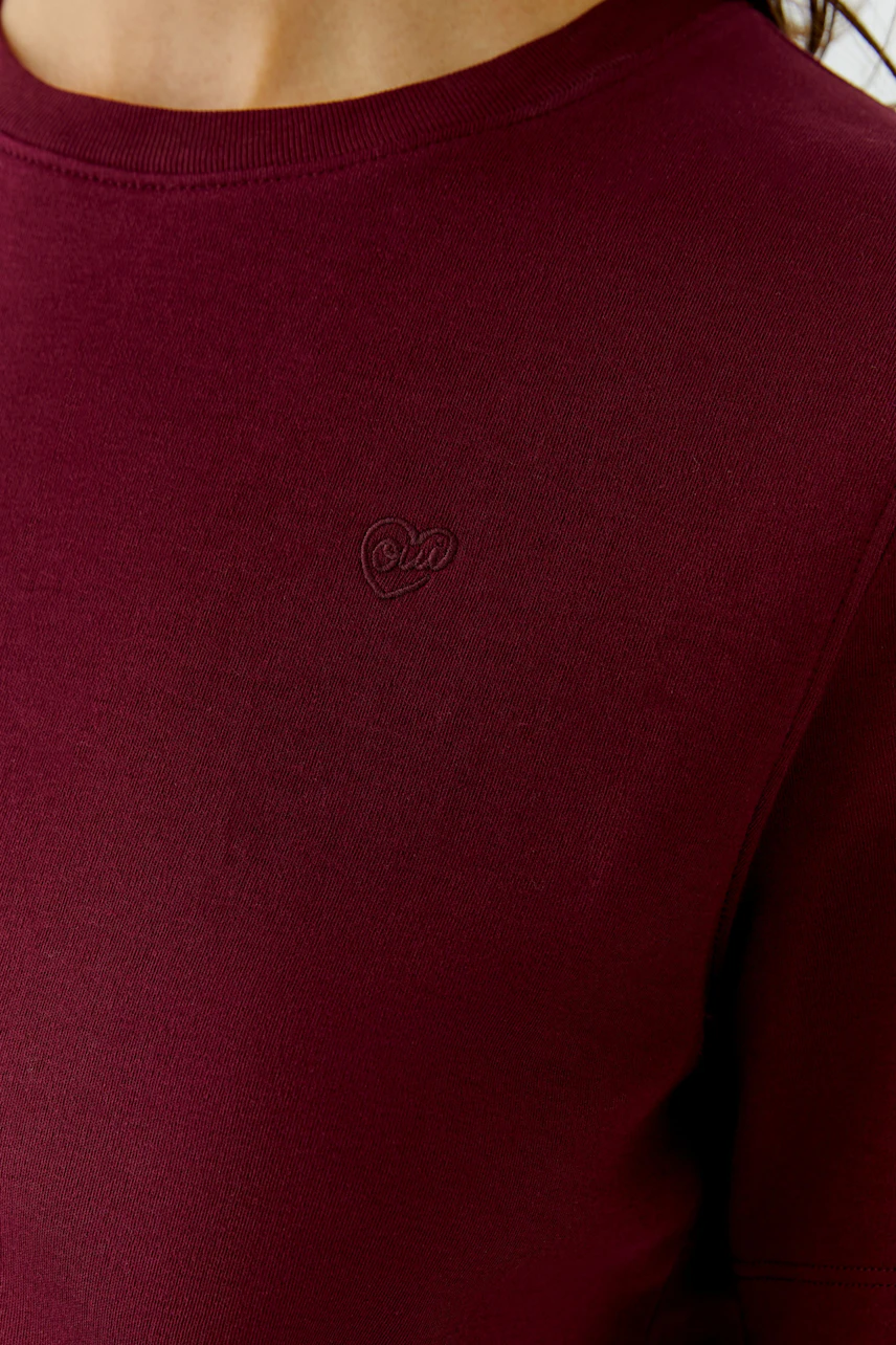 Bordeauxrotes Damen-T-Shirt: Frau trägt schlichtes T-Shirt mit kleinem Herz-Logo auf der Brust.