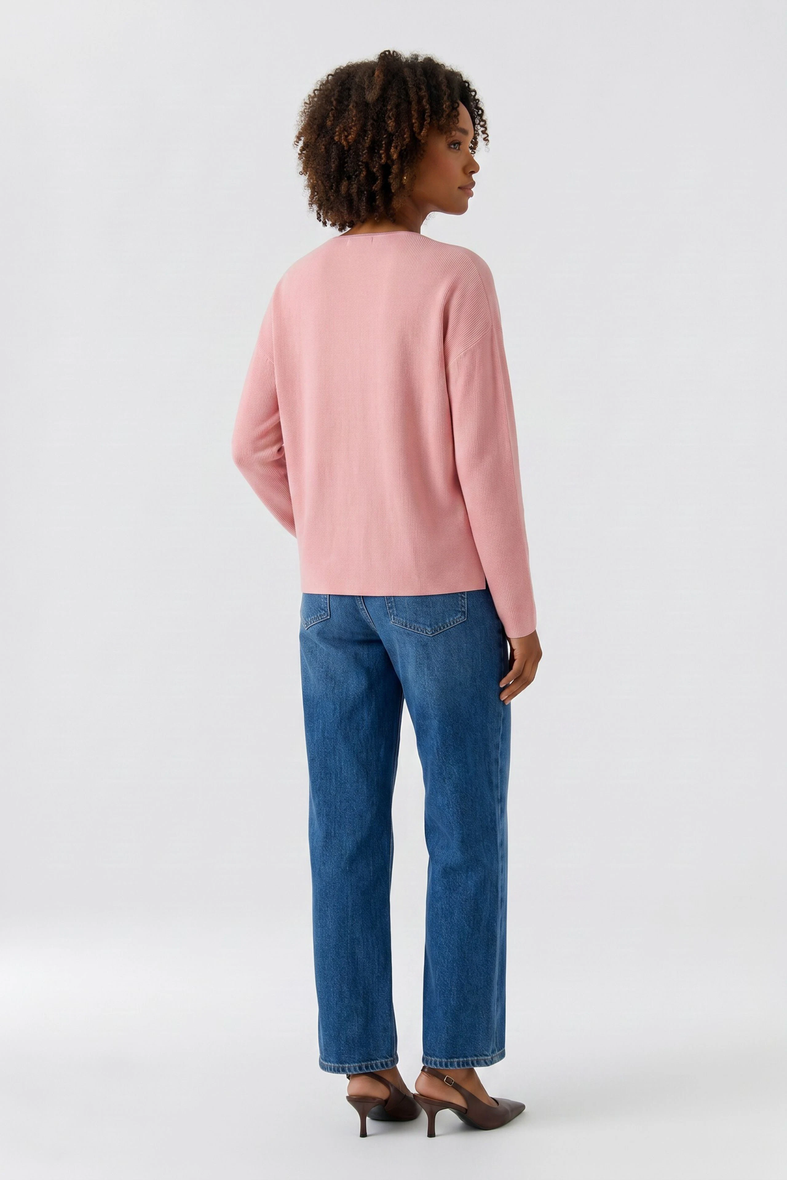 Casual women's pullover: Woman in a pink pullover and blue jeans, standing confidently.