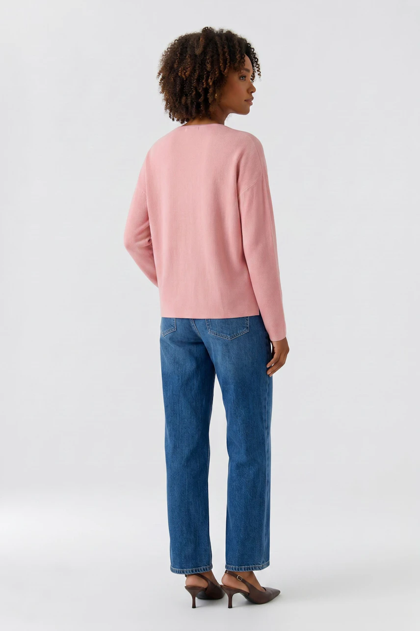 Casual women's pullover: Woman in a pink pullover and blue jeans, standing confidently.