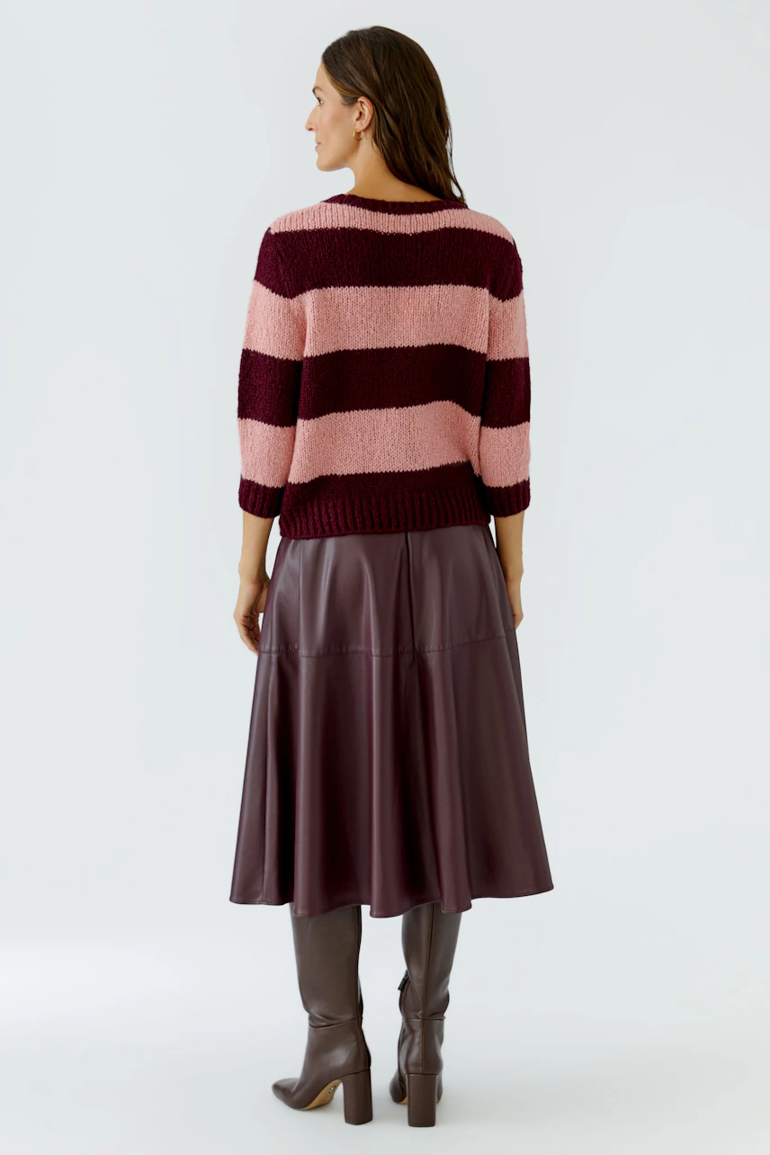 Frau im gestreiften Pullover in Rosa und Bordeaux, kombiniert mit braunem Rock und Stiefeln, von hinten.