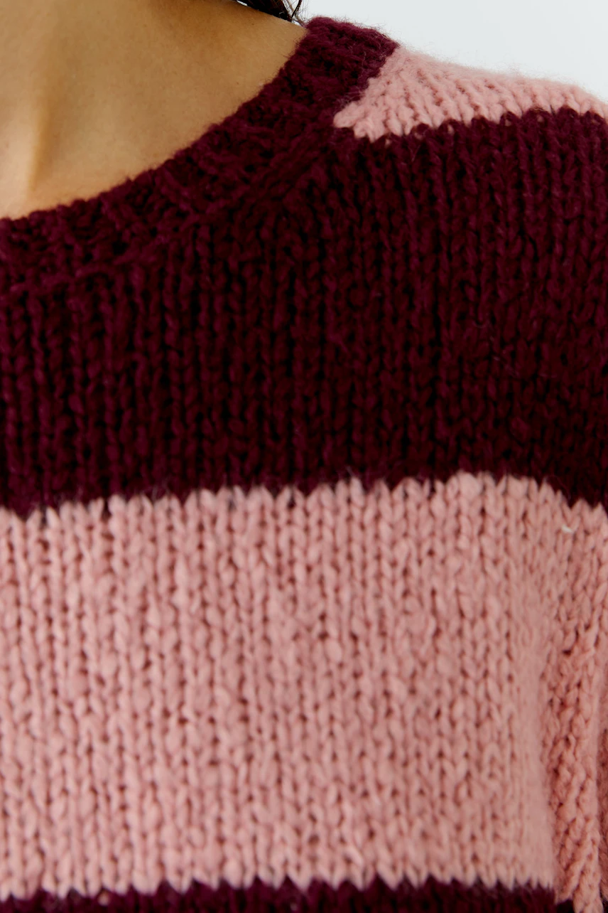 Frau trägt gestreiften Pullover in Rosa und Bordeaux. Grob gestrickt, ideal für kühle Tage.