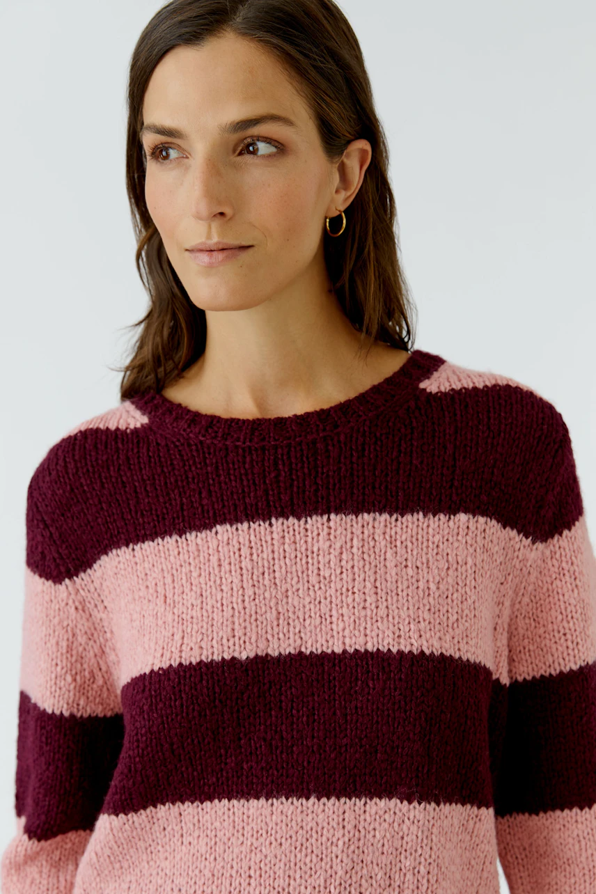 Frau im gestreiften Pullover: Rosa und bordeauxfarbene Streifen, lässiger Look, goldene Ohrringe.