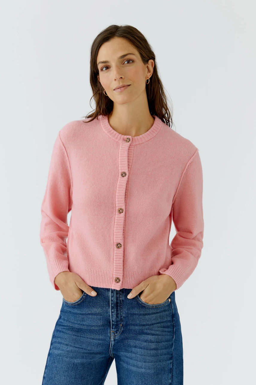 Frau in rosa Strickjacke: Lässige Passform, kombiniert mit blauen Jeans, wirkt modern und frisch.