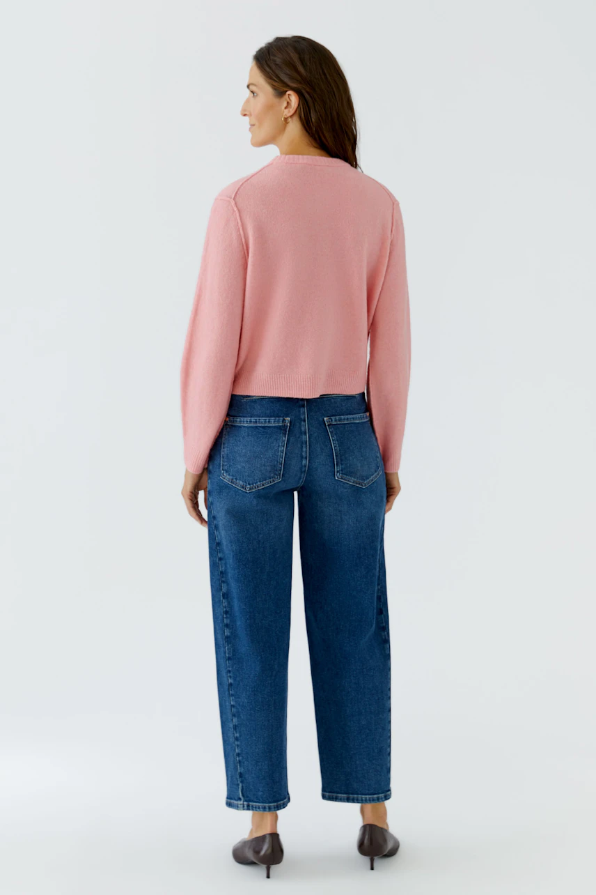 Frau in rosa Strickjacke und blauer Jeans, von hinten gesehen. Lässiger Look für den Alltag.