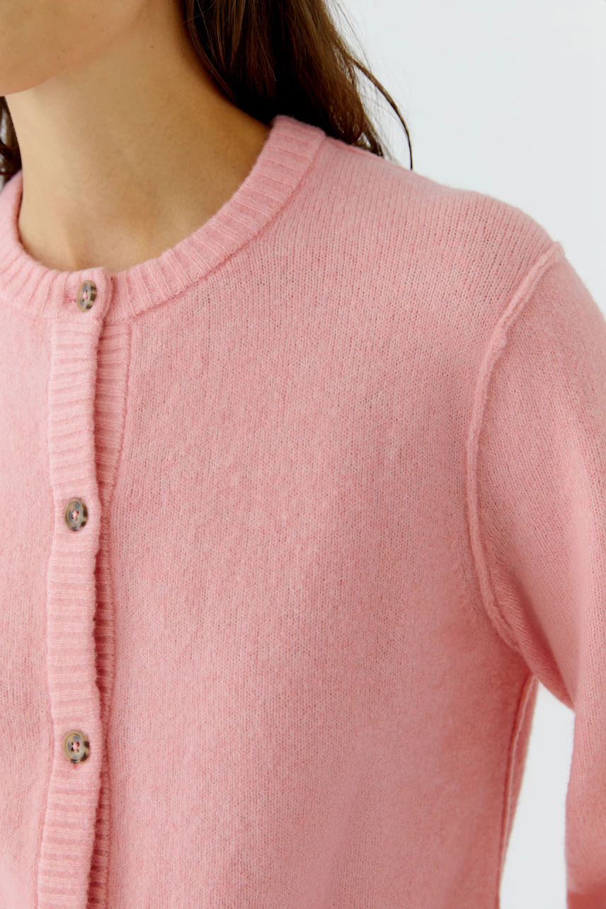 Frau in rosa Strickjacke: Nahaufnahme der Knopfleiste und des weichen Materials.