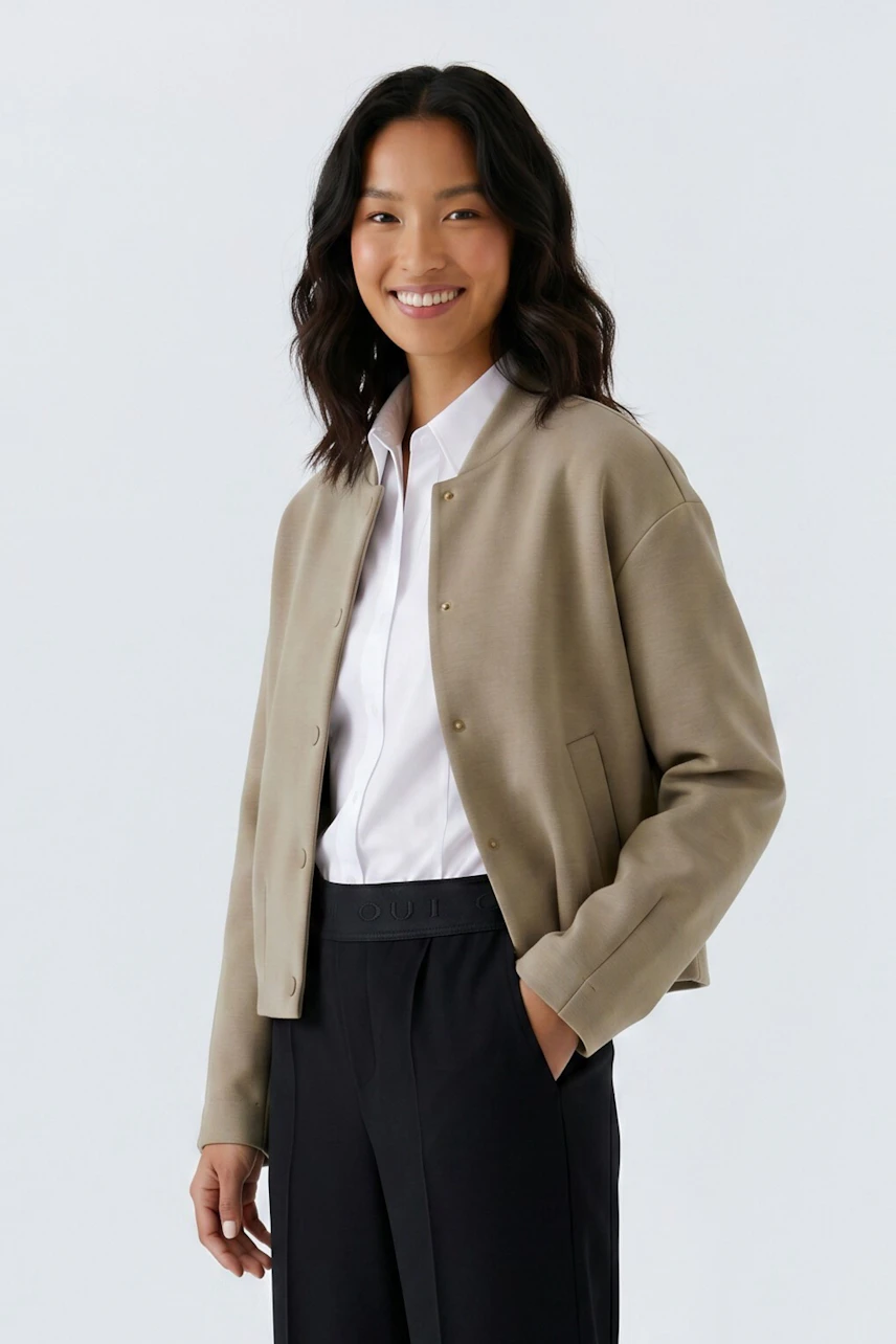 Casual blouson: Woman in beige blouson over white shirt, paired with black pants, smiling confidently.