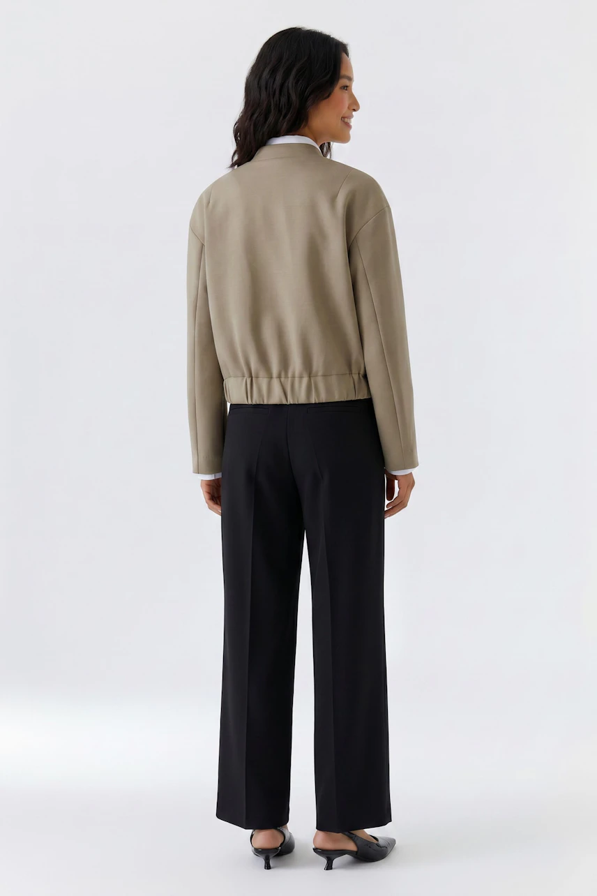 Casual blouson: Woman in beige blouson, black trousers, and heels, standing confidently.