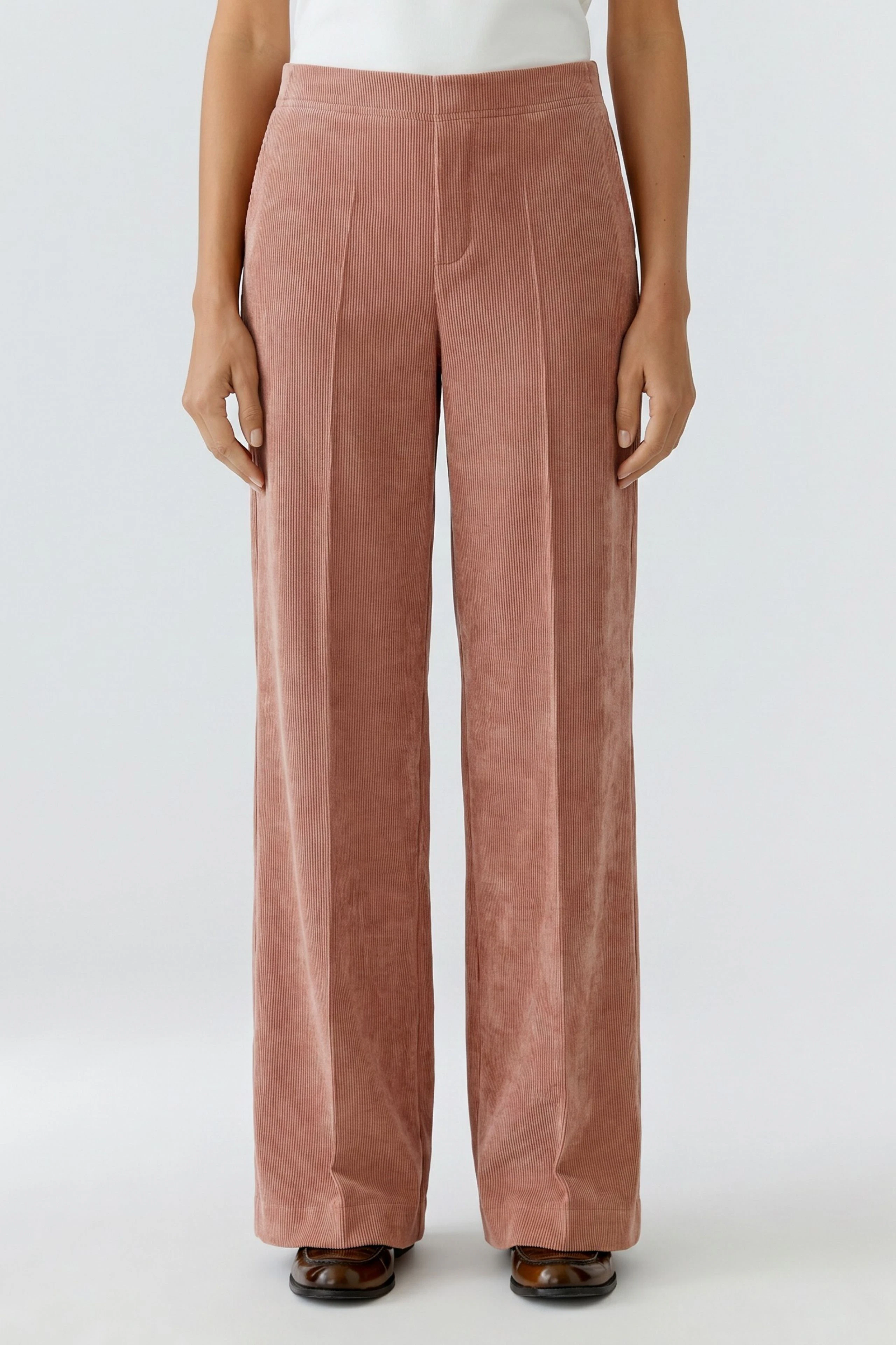 Casual corduroy pants: Woman in wide-leg, high-waisted pink corduroy pants, hands relaxed at sides.