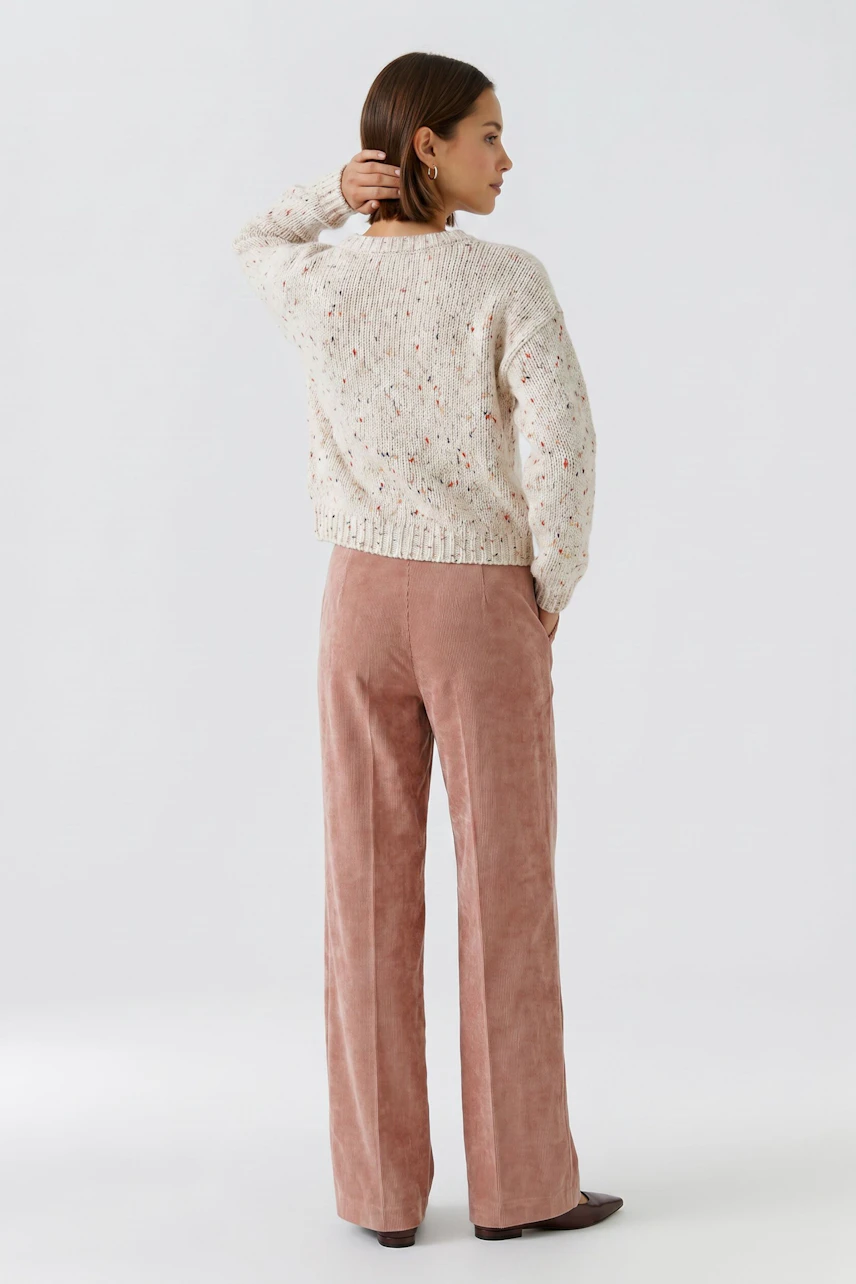Frau in rosafarbener Cordhose und cremefarbenem Pullover, Rückansicht. Lässiger Look für den Alltag.
