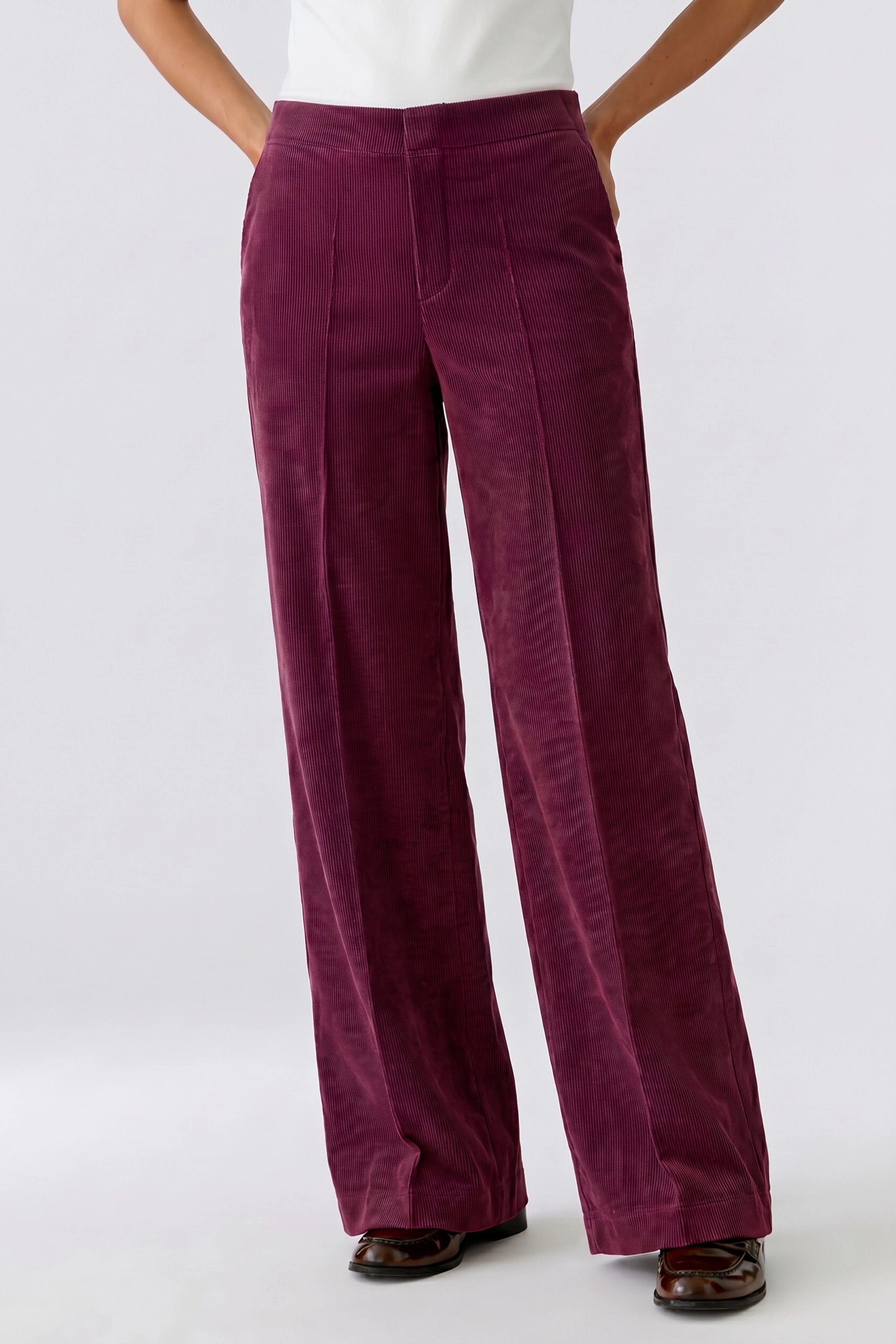 Woman in burgundy corduroy pants, white top. Relaxed fit, perfect for casual wear.