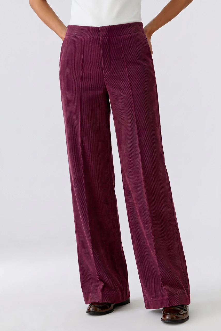 Frau in weinroter Cordhose: Lässiger Look mit weitem Bein und hoher Taille, kombiniert mit weißen Schuhen.