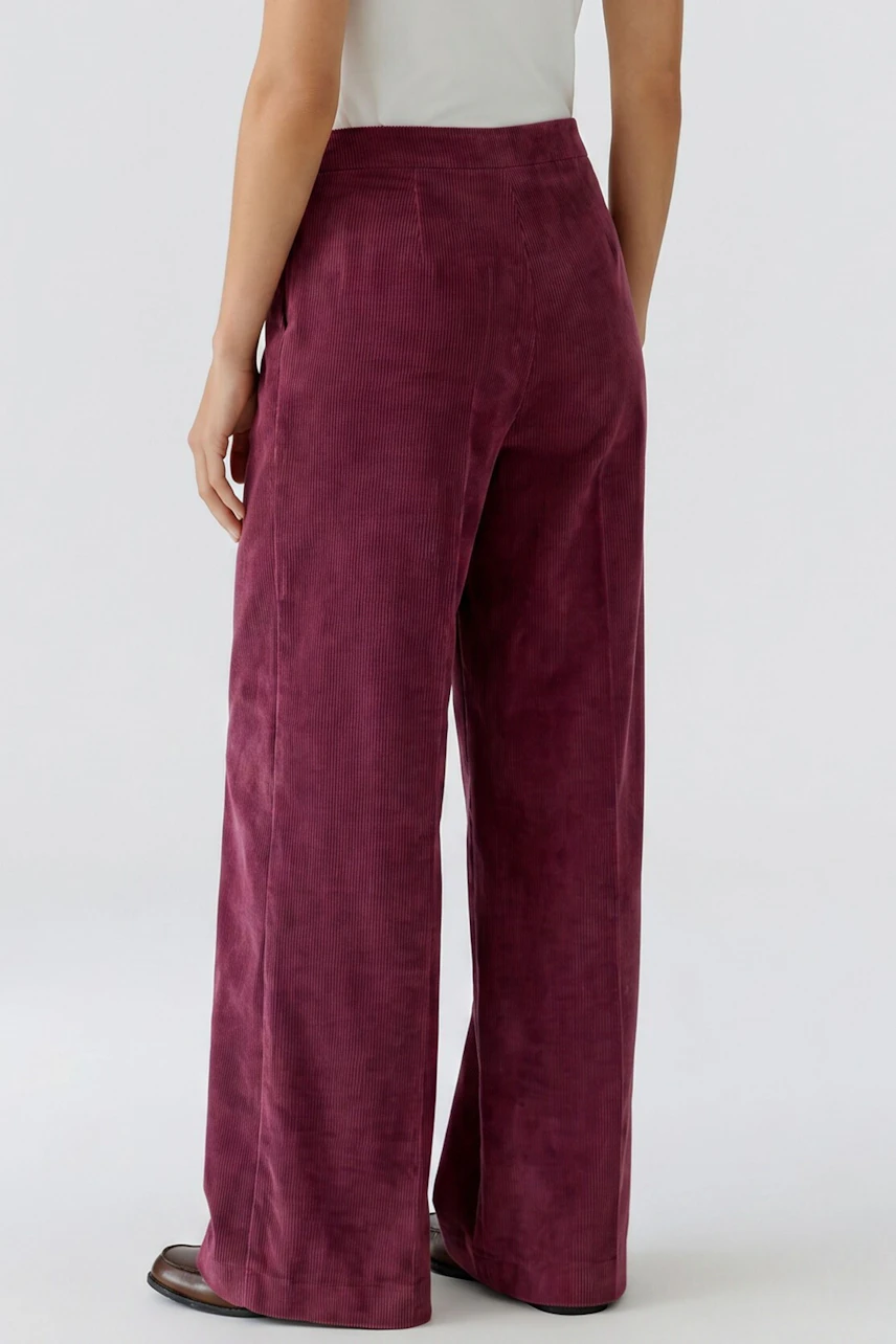 Frau in weinroter Cordhose, locker geschnitten, mit weißem Oberteil. Bequemer, lässiger Look.