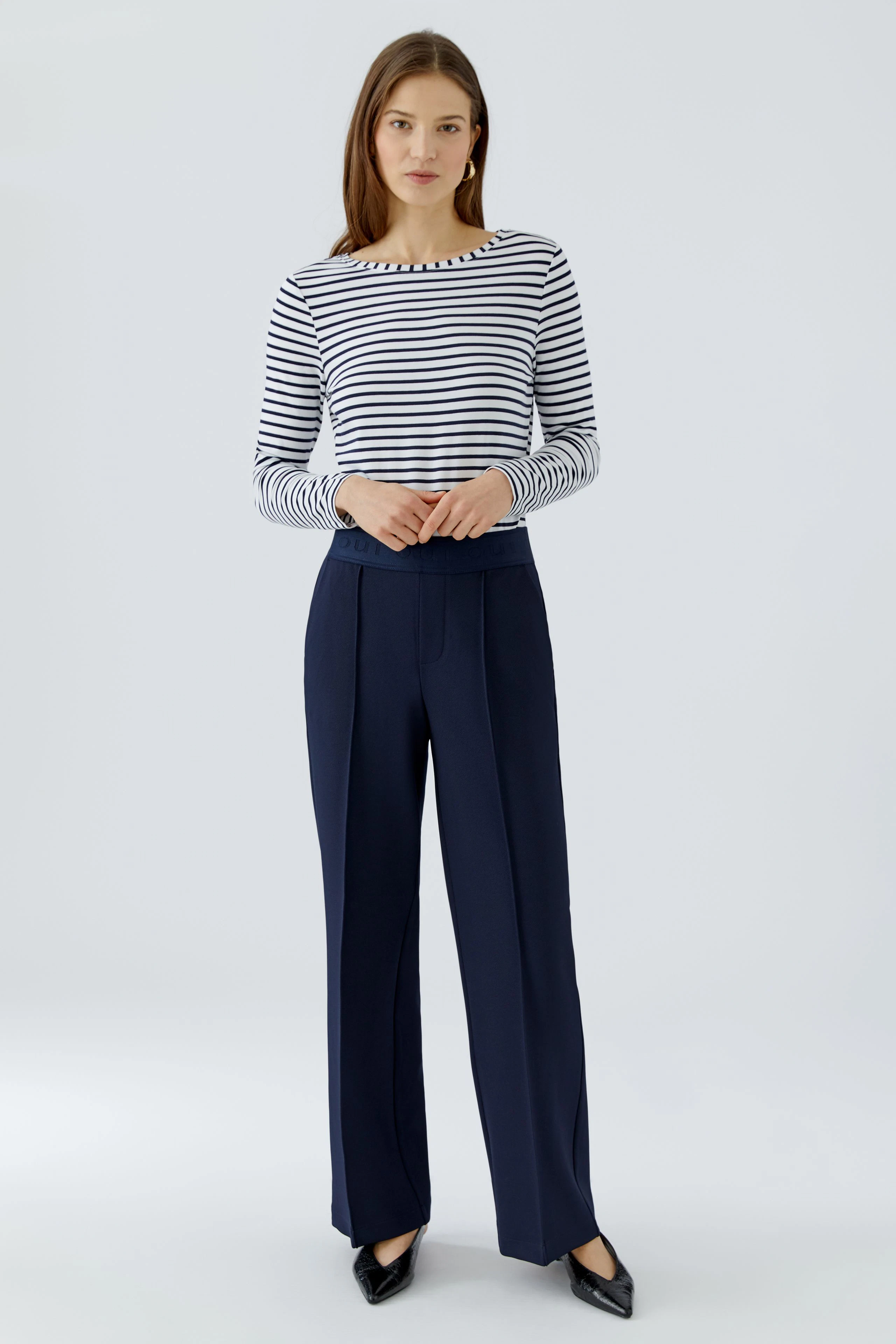 Woman in navy trousers and striped top, standing confidently. Focus on the trousers.