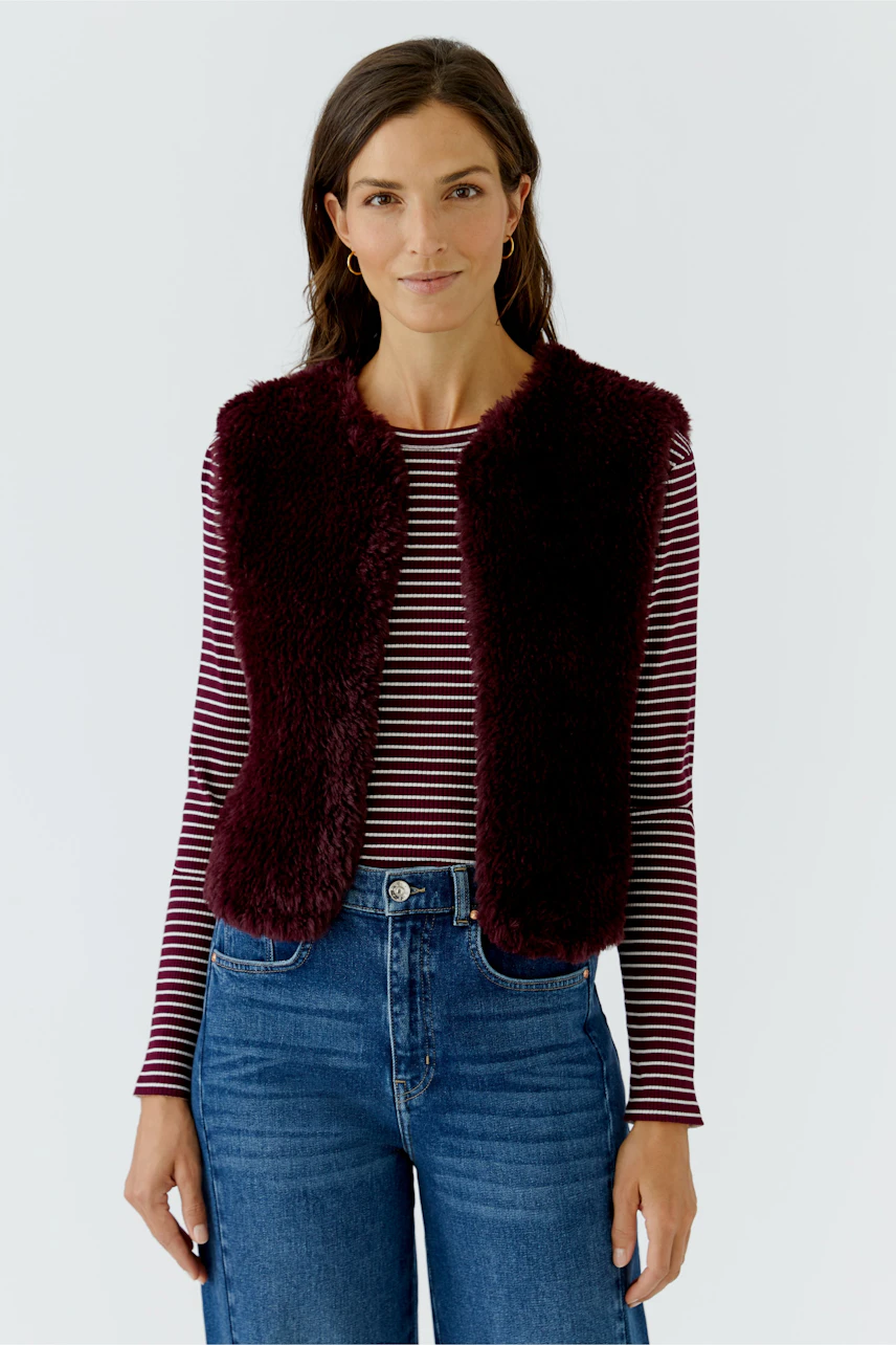 Woman in a cozy knit vest over a striped top and jeans, exuding casual style.