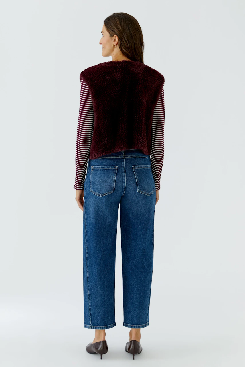 Woman in striped top and jeans wearing a burgundy knit vest, viewed from the back.