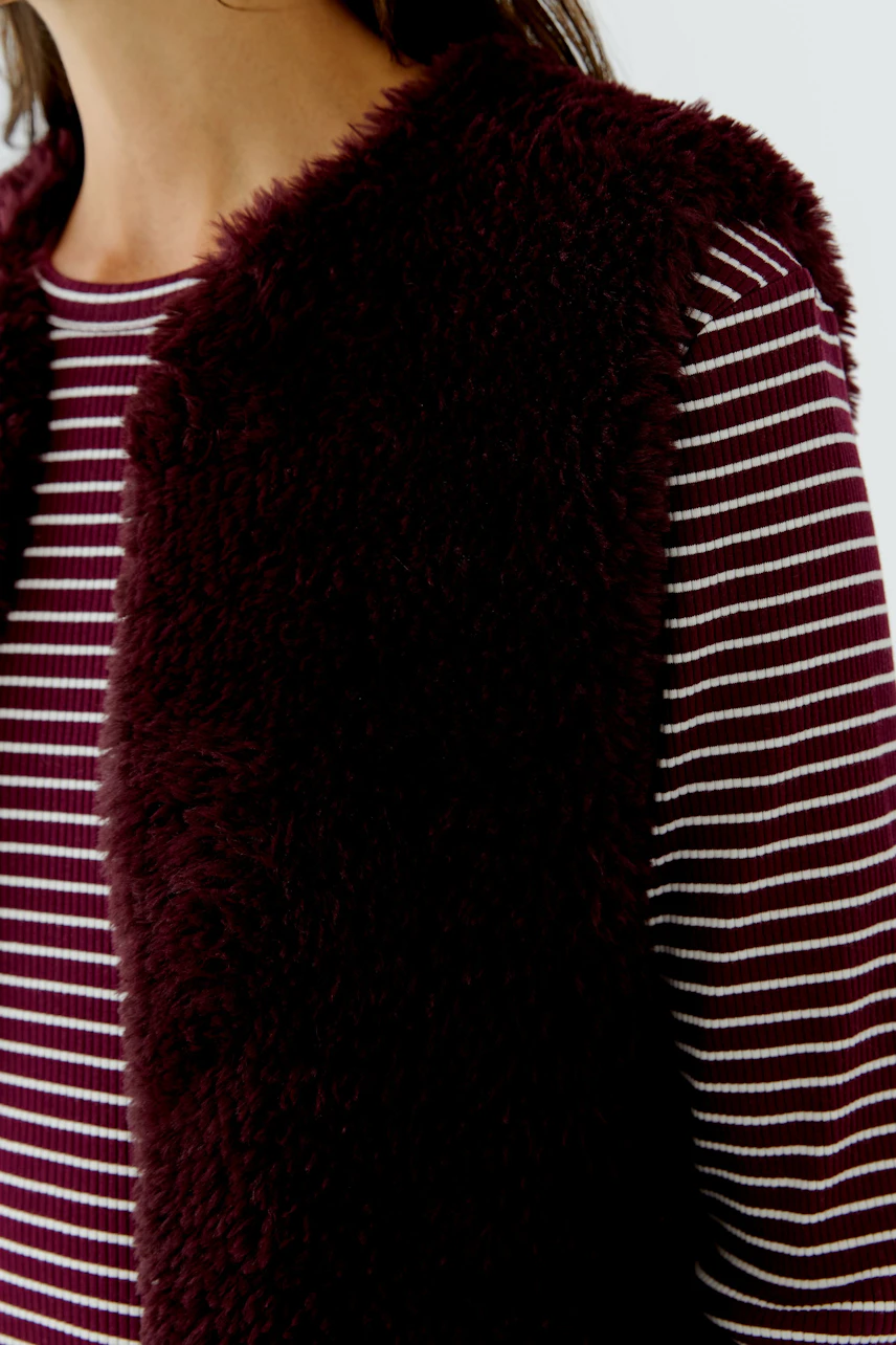 Woman in a fluffy knit vest over a striped pullover, showcasing casual style.