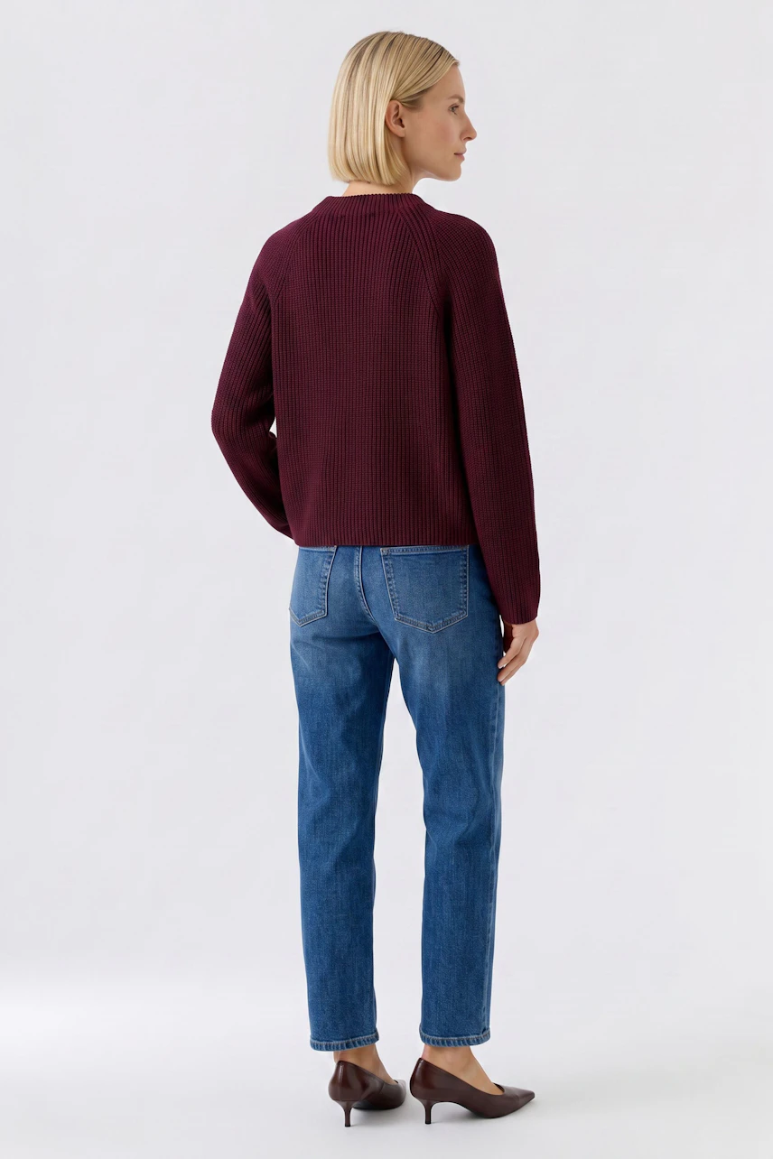 Casual women's pullover: Woman in a burgundy pullover and blue jeans, viewed from the back.