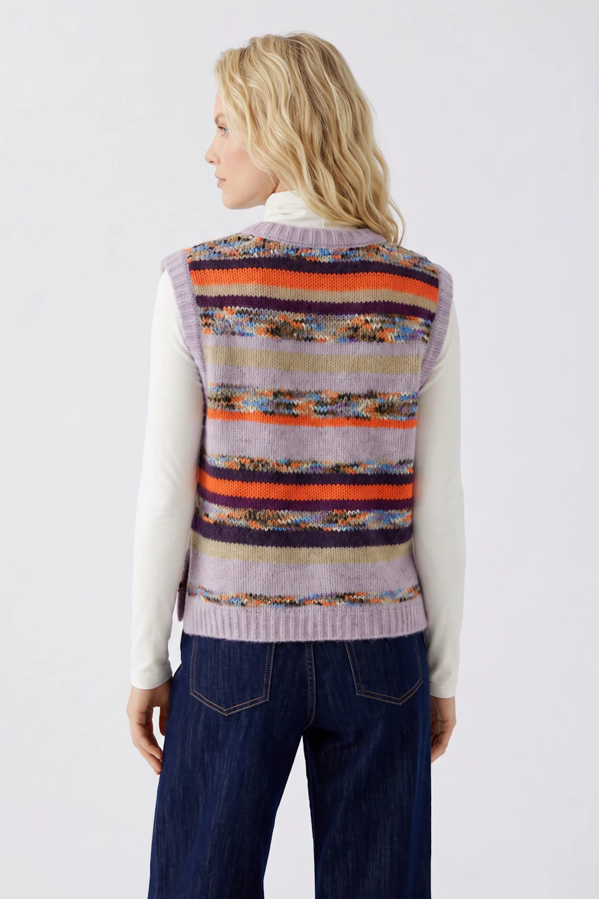 Frau im gestreiften Pullunder und weiter Jeans, seitlich stehend. Lässiger Look für den Alltag.
