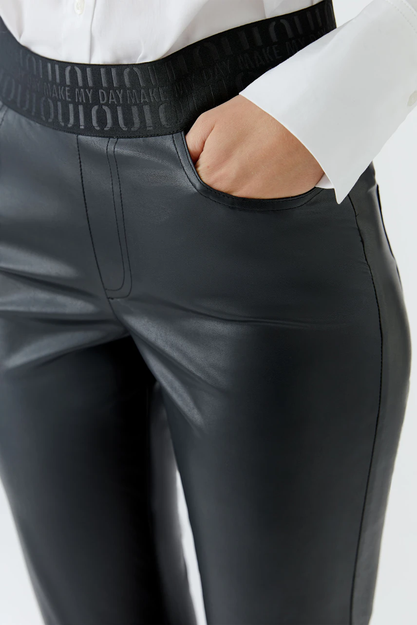 Lederimitathose: Frau in schwarzer Hose mit elastischem Bund und weißer Bluse, Hand in der Tasche.