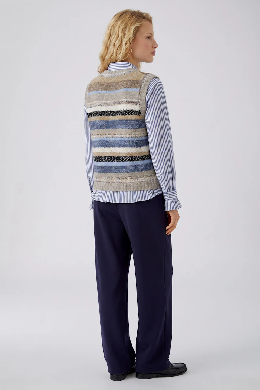 Striped pullover vest: Woman in a sleeveless knit vest with blue and beige stripes, paired with navy pants.
