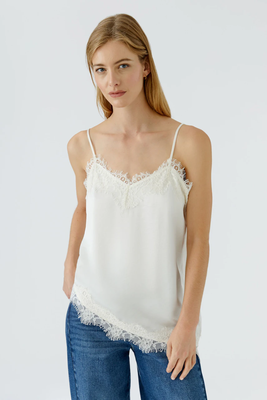 Damen-Top: Frau im weißen Spitzentop mit schmalen Trägern und blauer Jeans, schlicht und stilvoll.